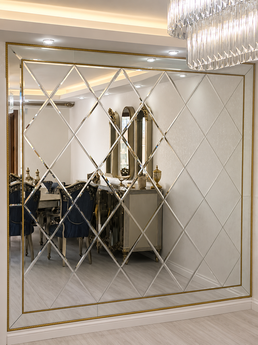 Large gold-accented diamond-pattern mirror wall reflecting an elegant dining room with a crystal chandelier and classical furniture.